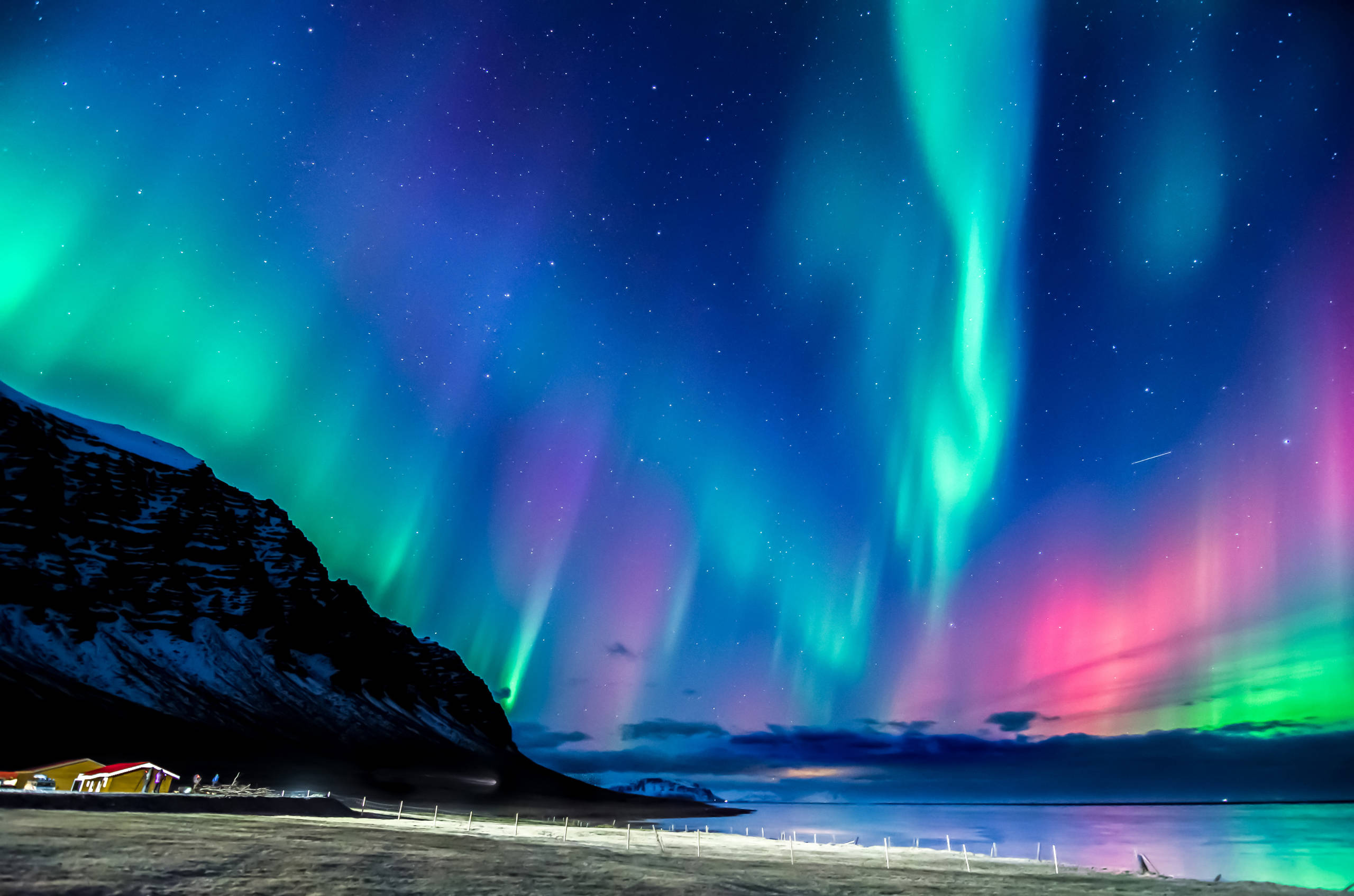 Northern lights over a small village, the ocean and surrounding mountains