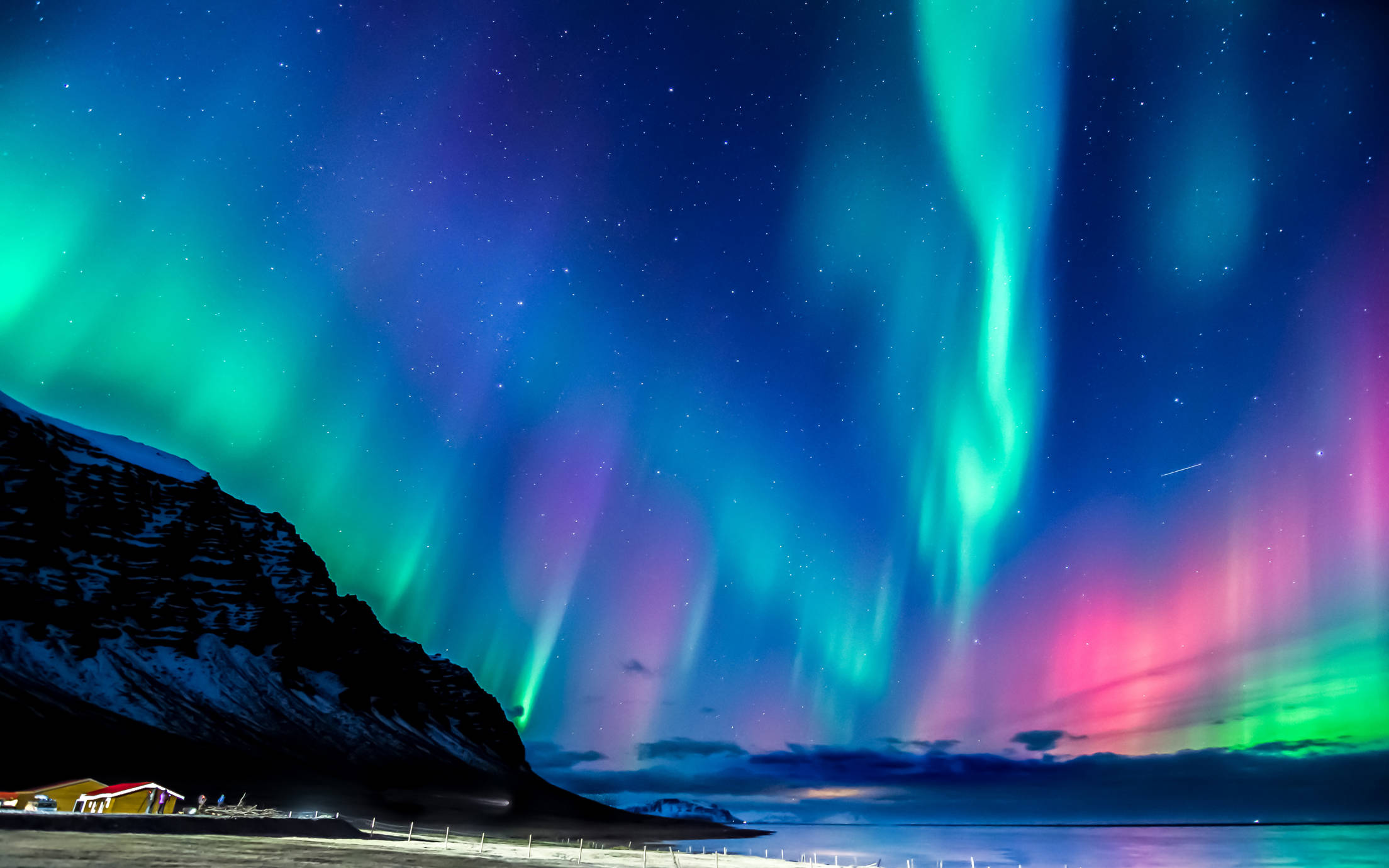 Northern lights over a small village, the ocean and surrounding mountains